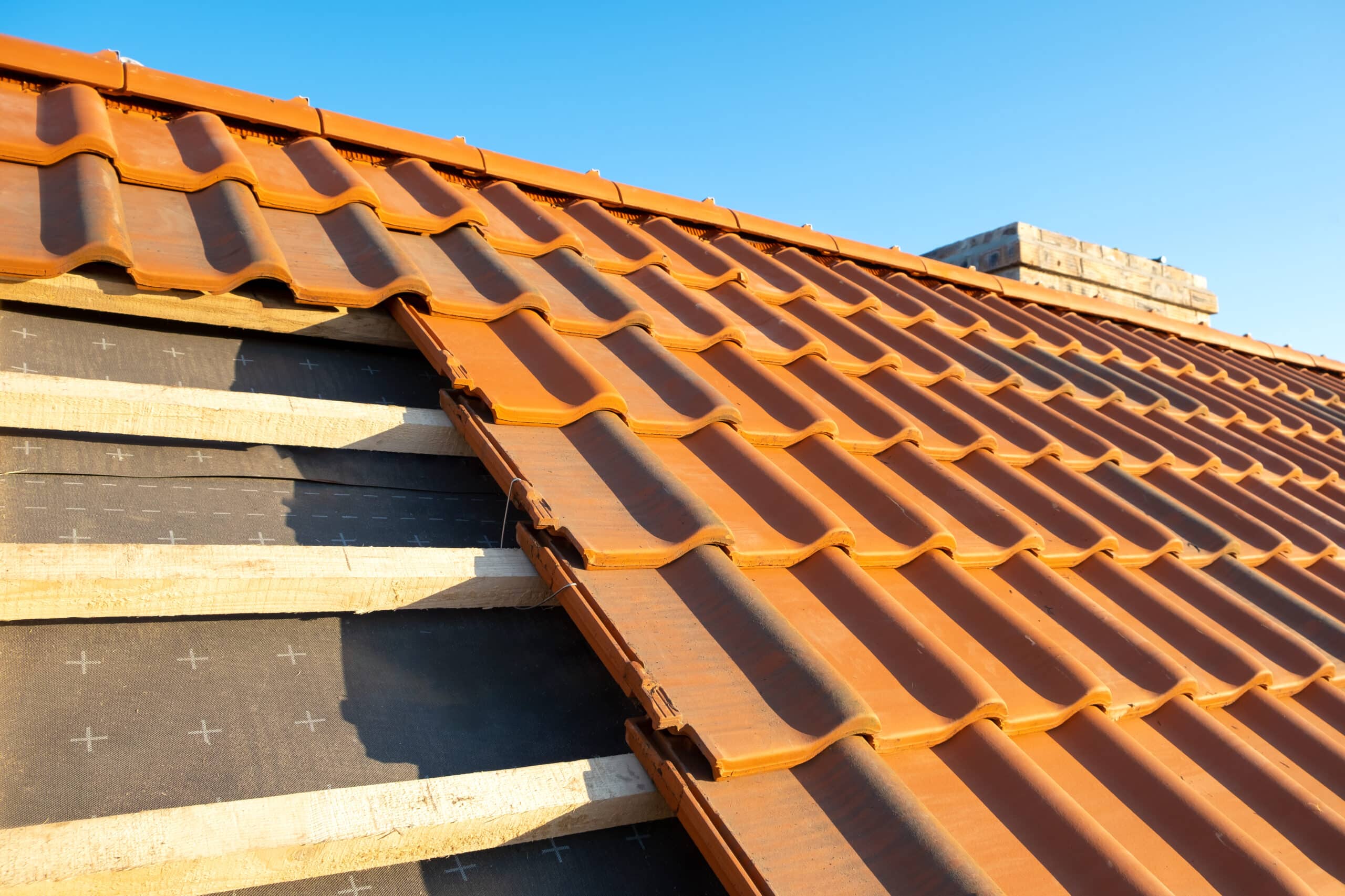 Overlapping rows of yellow ceramic roofing tiles mounted on wooden boards covering residential building roof under construction.